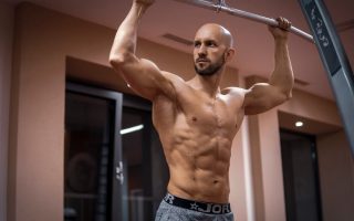 A bald, muscular man performing exercise on gym equipment indoors.