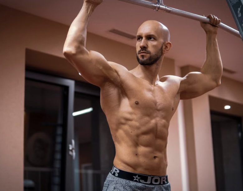 A bald, muscular man performing exercise on gym equipment indoors.
